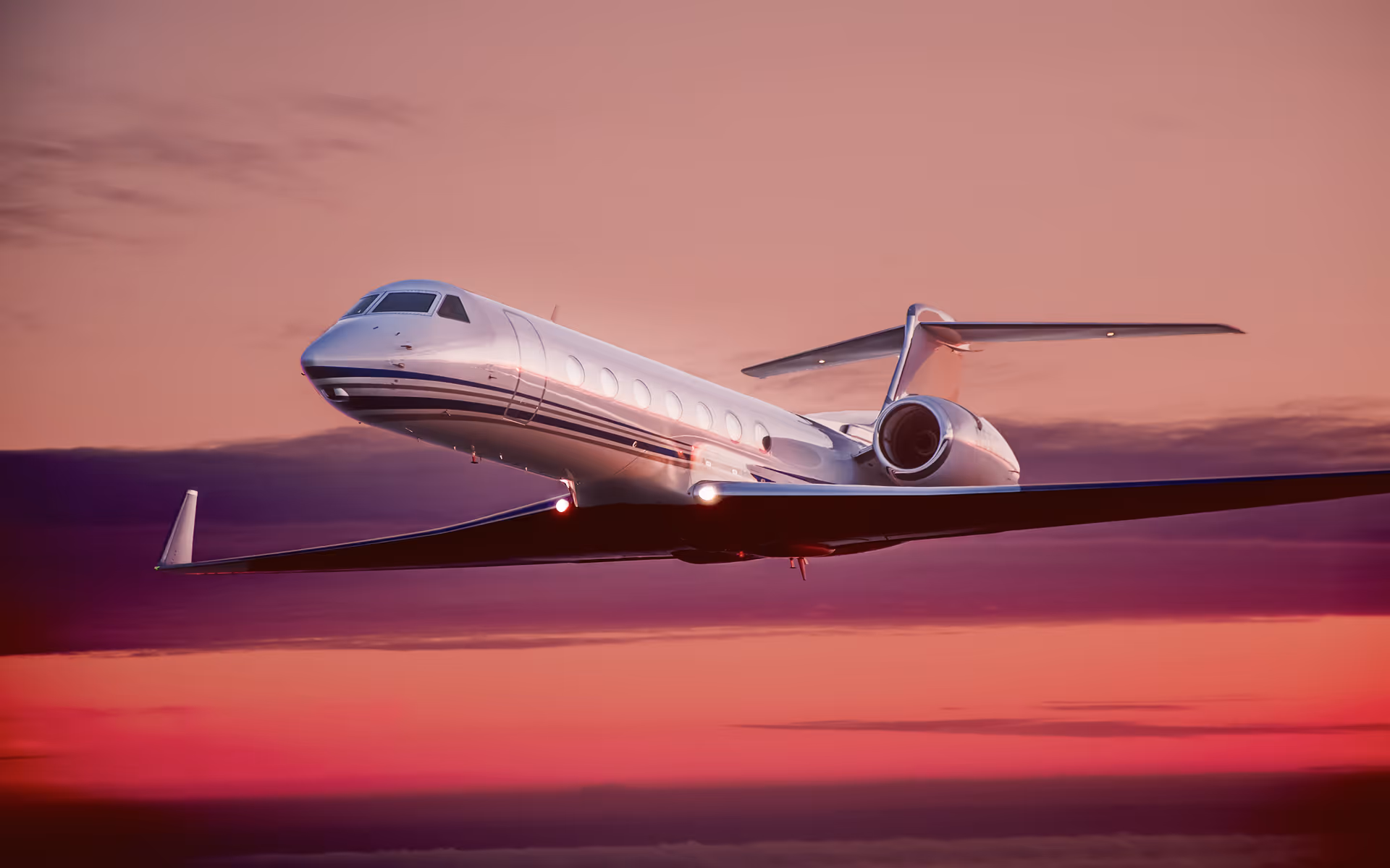 White private jet flying with lights on against a vibrant pink and purple sunset sky.