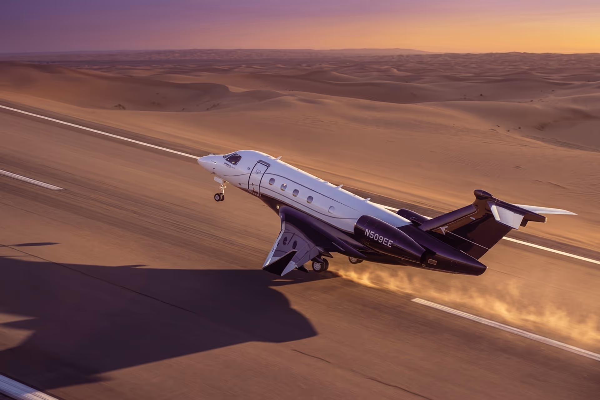 Private jet taking off from desert runway at sunset with dust trailing behind.