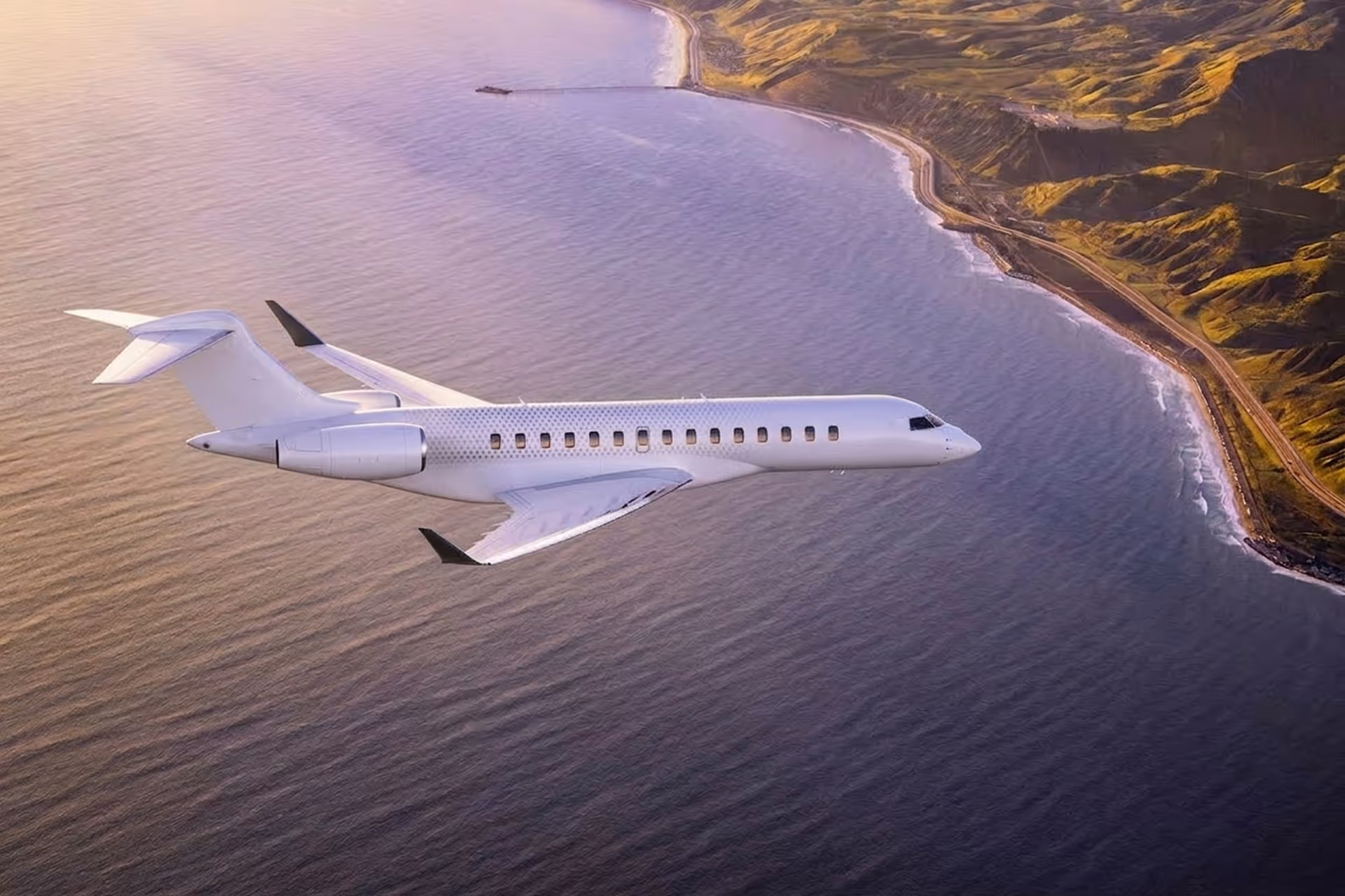 White private jet flying over a coastline with ocean and green hills at sunset.