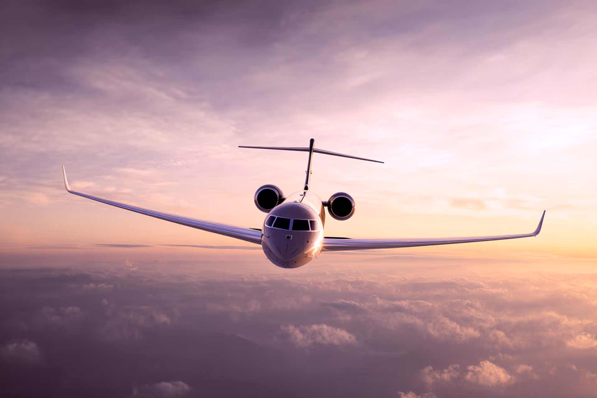Front view of a private jet flying above clouds during a purple and orange sunset.