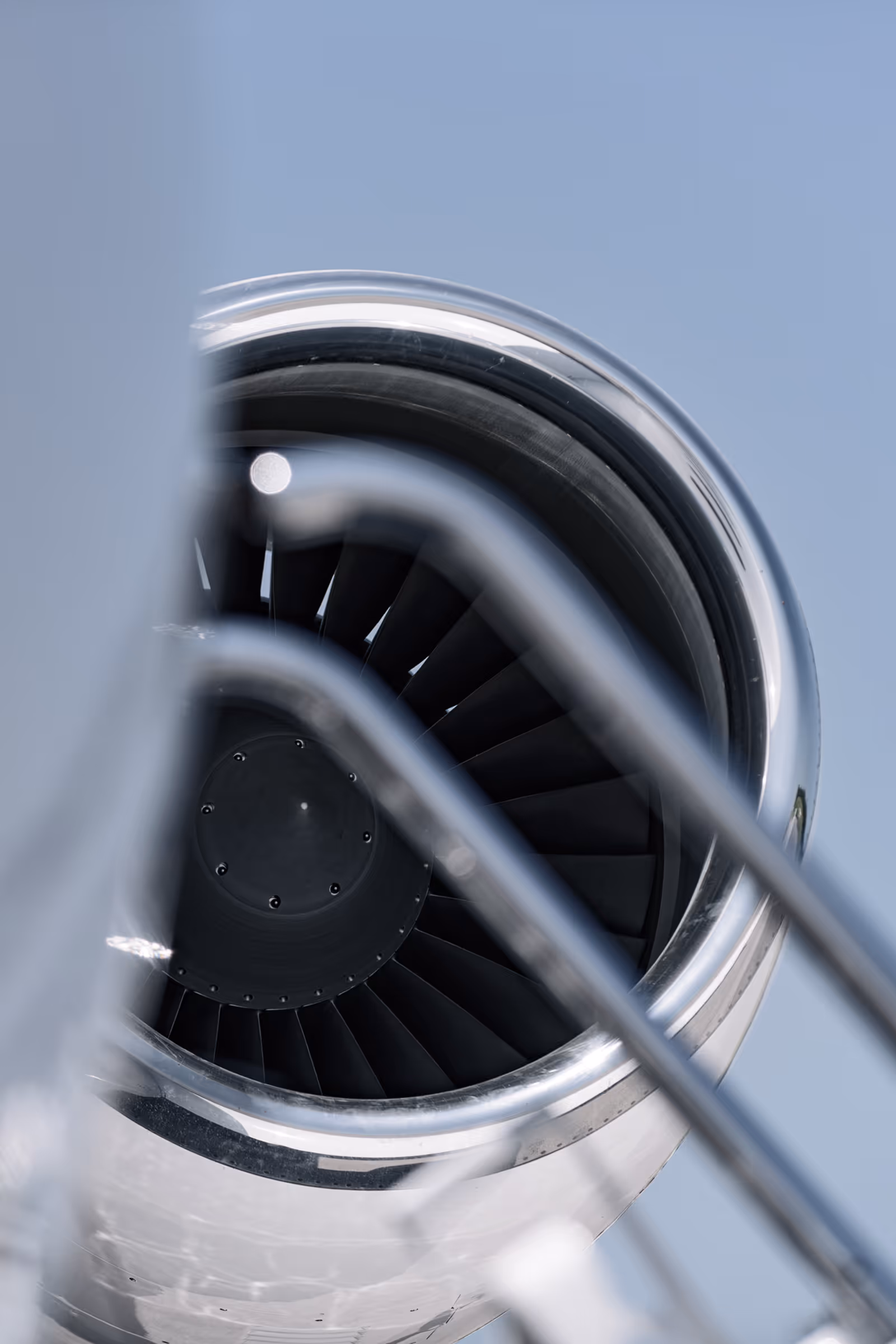 Close-up view of a jet engine turbine with metal railing in foreground against a clear blue sky.