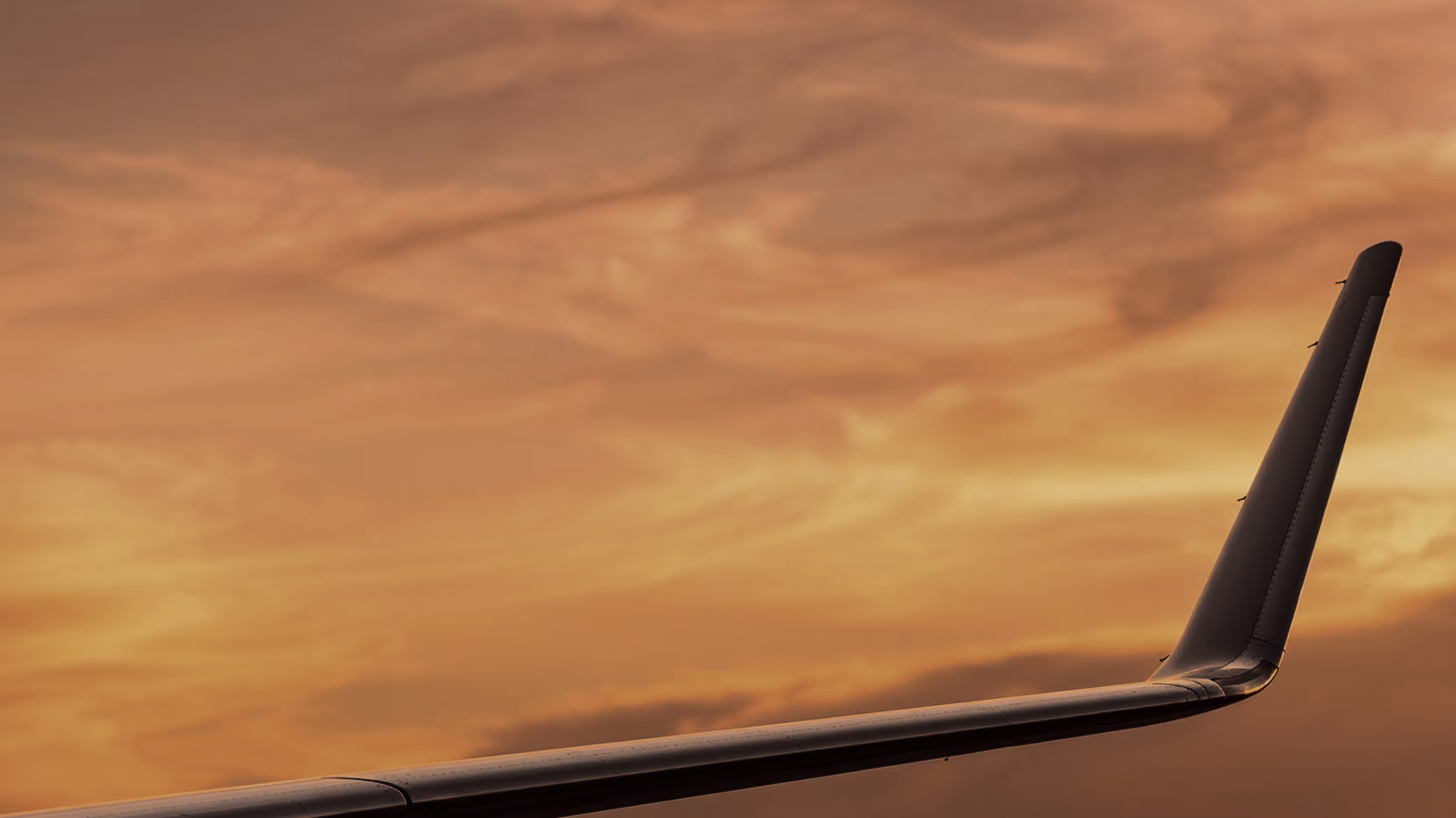 Airplane wing silhouetted against a golden sunset sky with scattered clouds.